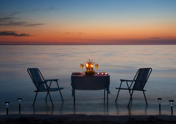 כסאות ושולחן שערוך בצורה רומנטית עם נר מול שקיעה בים