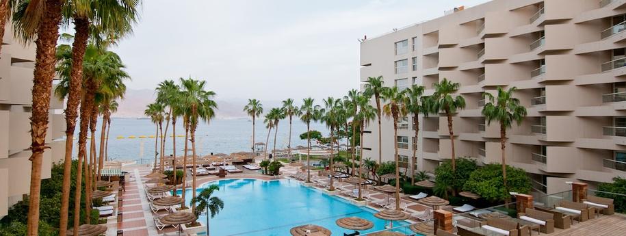 בריכת המלון אריאה באמצע המלון עצי דקל מיטות שיזוף ונוף לים