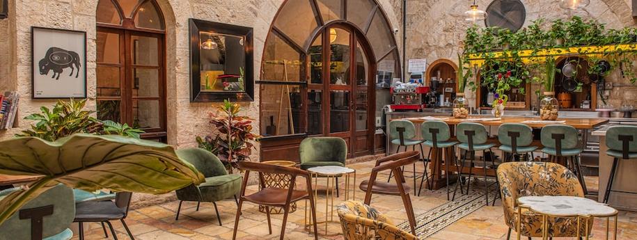 חצר מלון הבוטיק אלגרה עם כסאות שונים, בר , צמחייה ודלת עם מסגרת עץ וזכוכית שקופה