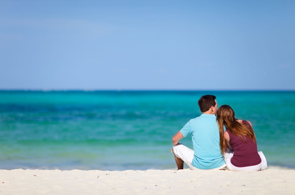 זוג יושב על חוף הים מחובקים עם הגב