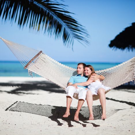 זוג יושב על ערסל עם נוף של ים ועצי דקל