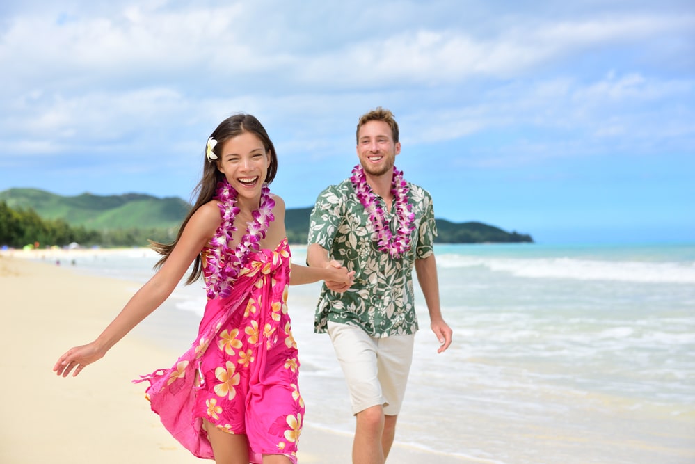 זוג מחויך רץ על החוף בהוואי עם שרשראות הוואיות