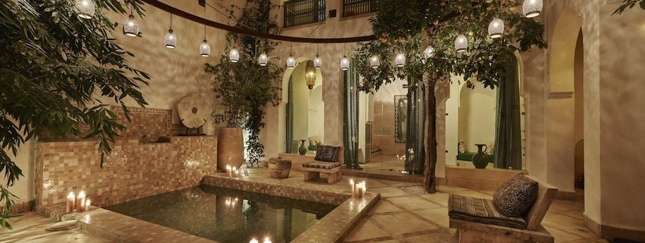 חצר מלון עם בירכה כסאות ישיבה נרות בקצוות של הבריכה צמחייה ועיצוב מרוקאי