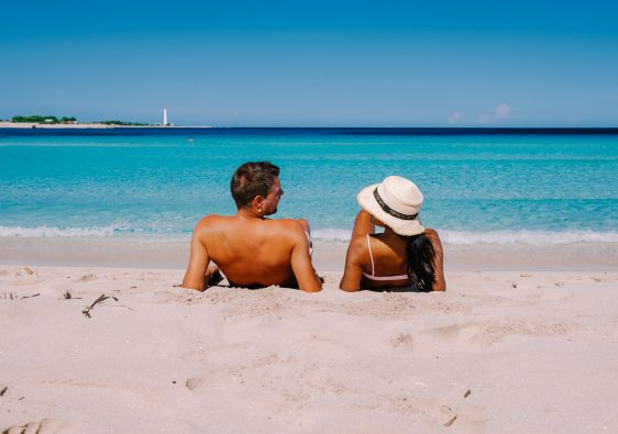 זוג שוכב על החול ומסתכל אחד לשניה בחוף הים בסיציליה