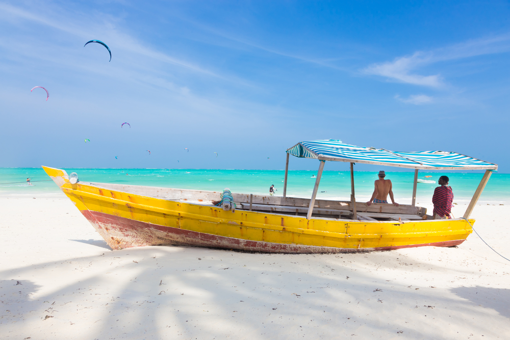 חוף עם חול לבן ומי טורקיז בזנזיבר עם סירה על החוף בצבע צהוב