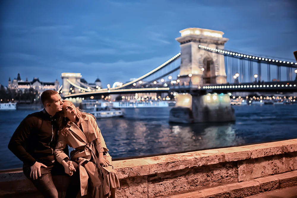 זוג יושב ליד אגם וגשר מואר בבודפשט בשעות הערב