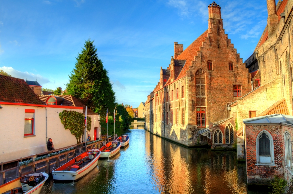 נהר באמצע העיר בבלגיה עם סירות בצד אחד ובנינים עתיקים בצד השני