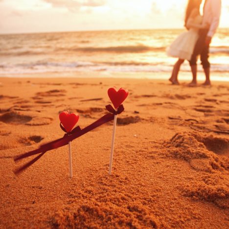 מקלות עם לב בחול ובנוך ים וזוג מתחבק