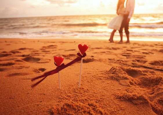 מקלות עם לב בחול ובנוך ים וזוג מתחבק